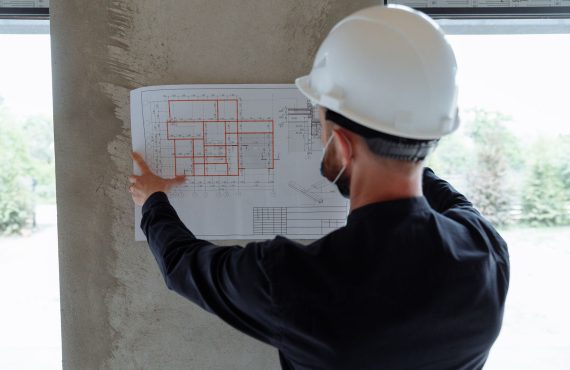 Engineer in hardhat reviewing architectural floor plans at construction site.