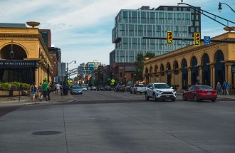 Busy city intersection with cars, buildings, and pedestrians on a clear day.