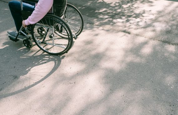 A person in a wheelchair navigating a sunlit road with tree shadows. The image captures a moment of mobility and independence.