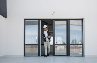 A professional architect walks out of a modern building holding house plans, symbolizing construction and development.