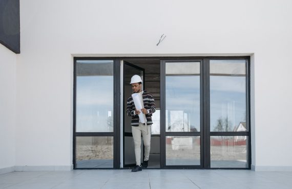A professional architect walks out of a modern building holding house plans, symbolizing construction and development.