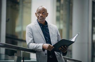 Confident African American manager in formal suit carrying folder with papers and looking away in soft daylight