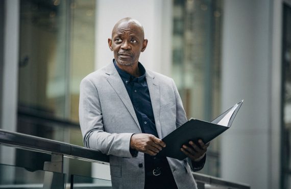 Confident African American manager in formal suit carrying folder with papers and looking away in soft daylight