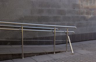Close-up of a metal handrail and concrete ramp for accessibility in an urban setting.
