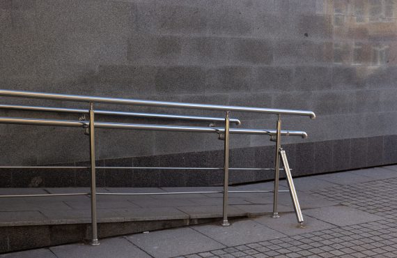 Close-up of a metal handrail and concrete ramp for accessibility in an urban setting.