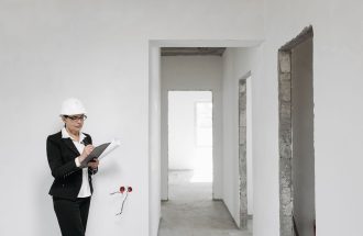 Woman architect in helmet and suit inspecting unfinished interior. White walls signify new construction.