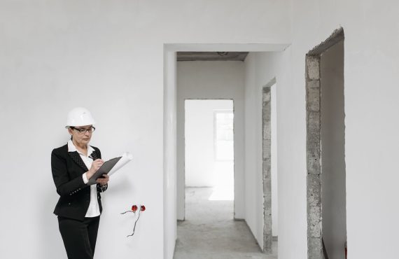 Woman architect in helmet and suit inspecting unfinished interior. White walls signify new construction.