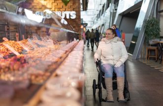 A woman in a wheelchair browsing a nut stall at an indoor market in Rotterdam, Netherlands.