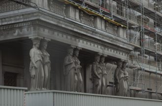 Neoclassical statues with scaffolding on a historic Vienna building reflects ongoing renovations.