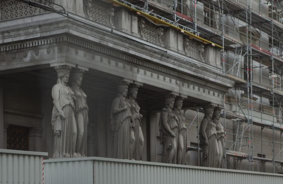Neoclassical statues with scaffolding on a historic Vienna building reflects ongoing renovations.