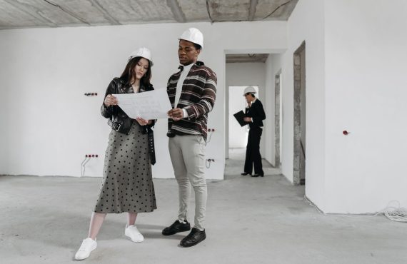 Two architects examine blueprints in a partially finished building while discussing design plans.